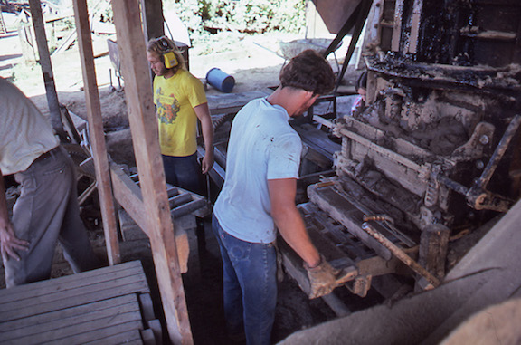 View of the worker removing the loaded brick mold from the brick press. 